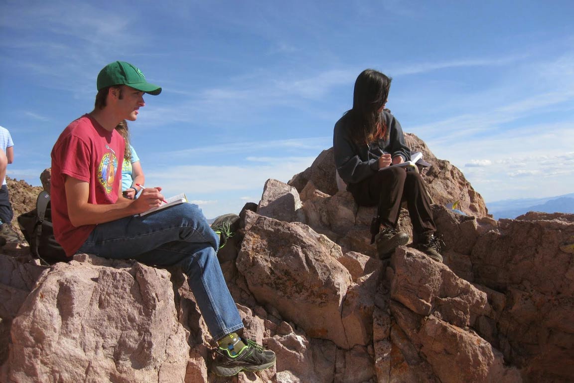 Two students perched on boulders taking notes