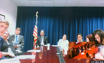 Screenshot of a web conference of people sitting around a conference table with American flag in background